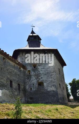 Eine mächtige Steinmauer einer mittelalterlichen Festung mit vielen Schlupflöchern und Schießscharten. In der Ferne ein großer Turm mit Dach Stockfoto