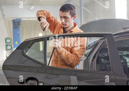 Auto-Service-Mitarbeiter demontiert Autotür für die Reparatur, Restaurierung. Stockfoto