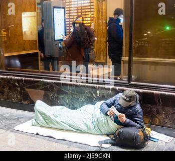 Obdachloser, der in einem Schlafsack auf der Straße liegt und vor dem McDonalds Restaurant liest. Winter Madrid, Spanien, Europa Stockfoto