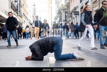 Ein Mann auf den Knien und mit dem Kopf auf den Boden, mit einem Plastikbecher, der um Geld bettelte, im Zentrum von Madrid, Spanien Stockfoto