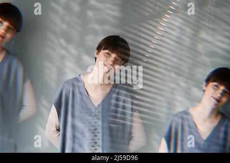 Mehrere Aufnahmen einer lächelnden hübschen Frau mit kurzen Haaren, die mit den Händen hinter der Wand steht Stockfoto