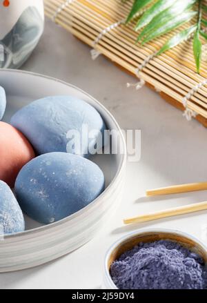 Eine Schüssel japanischer Mochi mit Essstäbchen und Holzmatte auf weißer Arbeitsplatte. Konzept eines traditionellen japanischen Desserttisches auf dem Küchentisch. Stockfoto