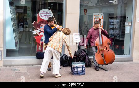 Eine Frau, die Geld für Cello- und Geigenspieler wirft Musiker Straßenmusiker in der Straße von Sevilla, Andalusien, Spanien Stockfoto