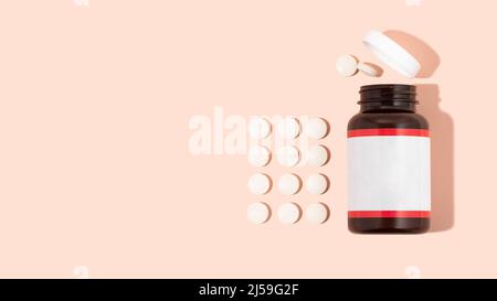Weiße Vitamine in Pillen und Glasflasche auf rosa Hintergrund. Wenige Tablets. Gesunde Immunität Konzept Zusammensetzung. Wellness, Lifestyle. Draufsicht Stockfoto
