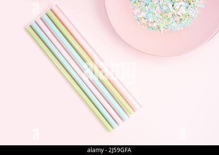 Trinkhalme und Teller voller Mikroplastik auf rosa Hintergrund. Auswirkungen von Mikroplastik auf die Lebensmittelkette. Die Idee der Mikroplastik Verschmutzung. Stockfoto