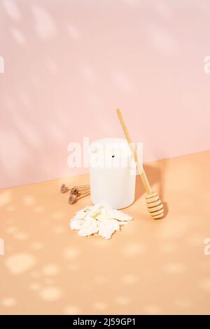 Duftkerze aus biologischem Sojawachs, Docht in einem weißen Keramikglas auf einem beige-rosa Hintergrund. Trendy diy, handgemachtes Konzept. Minimalismus. Isometrische Projektion Stockfoto
