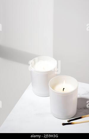 Brennende aromatische Kerze aus Sojawachs auf weißem Hintergrund mit einem schönen Schatten. Ökologische und vegane Kerzen und Streichhölzer auf einem Marmortisch Stockfoto