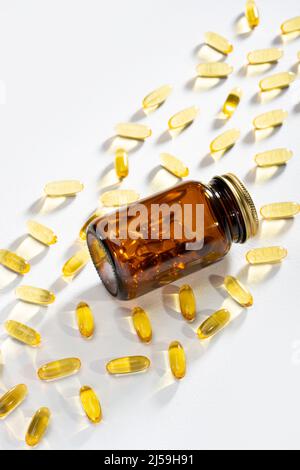 Sonnenlicht durchdringt eine Flasche mit Pillen und Omega-3 Kapseln, die auf weißem Hintergrund liegen. Ätzes Licht. Fischöl-Weichtiere. Medizinische Unterstützung Stockfoto