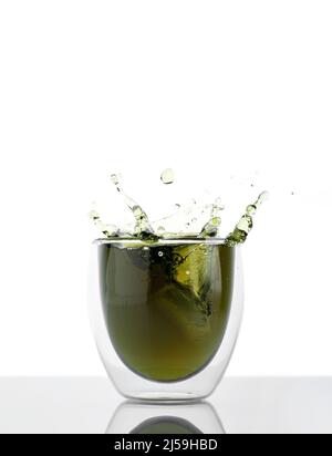 Glas Wasser mit Chlorophyll-Extrakt vor weißgrauem Hintergrund. Flüssiges Chlorophyll in einem Glas Wasser mit Spritzer. Konzept von Superfood Stockfoto