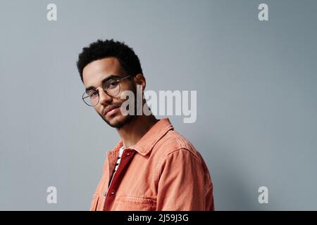 Porträt des Inhalts schöner junger afroamerikanischer Kerl in hellem Hemd vor grauem Hintergrund posiert Stockfoto