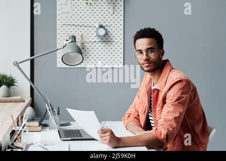 Porträt eines seriös selbstbewussten jungen gemischten Rennbüros in Brillen, die mit einem Dokument im modernen Büro sitzen Stockfoto