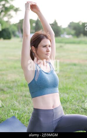 Junge sportliche Frau führt Übungen in der Natur. Frau praktiziert Yoga im Park. Gesunder Lebensstil Stockfoto