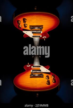Schönes Produktfoto von zwei rot-orange-braunen Cherry Sunburst Solid Body E-Gitarren auf einem dunklen (schwarzen) Hintergrund. Eine Gitarre gespiegelt Stockfoto