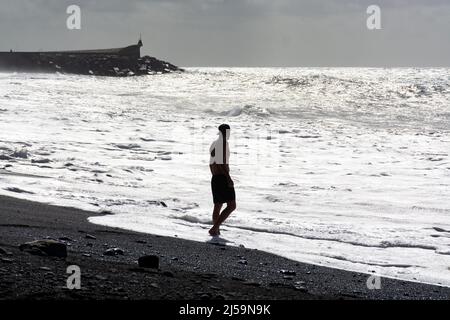 Ein nicht identifizierter Erwachsener spielt mit kaltem ozeanischem Wasser und Steinen, die am schwarzen Lavastrand auf der Insel La Palma, Kanarische Inseln, Spanien, springen Stockfoto