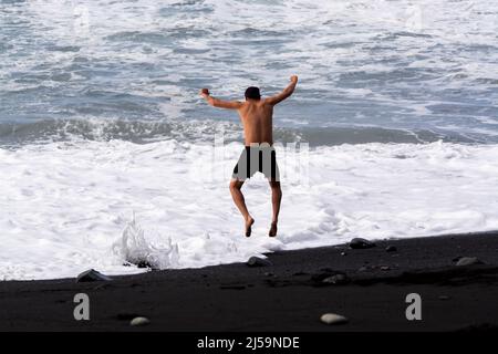 Ein nicht identifizierter Erwachsener spielt mit kaltem ozeanischem Wasser und Steinen, die am schwarzen Lavastrand auf der Insel La Palma, Kanarische Inseln, Spanien, springen Stockfoto
