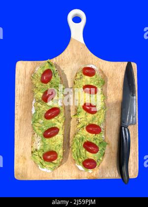 Sandwich mit Mayonnaise, Avocado und Kirschtomaten und einem Messer auf einem Holz auf blauem Hintergrund Stockfoto
