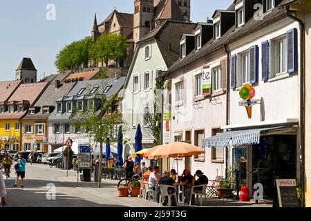 Breisach, Deutschland - April 2022: Menschen sitzen vor einem Café an der Hauptstraße durch die Stadt. Im Hintergrund befindet sich der Stephansdom Stockfoto