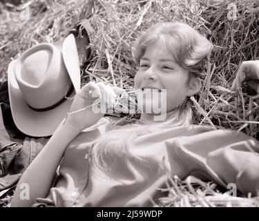 1950S LÄCHELNDES TEENAGER-MÄDCHEN, DAS AUF EINEM HEUHAUFEN LIEGT UND AUF EINEM STÜCK STROH IM MUND UND COWBOYHUT KAUT NEBEN IHR - J11681 HAR001 HARS JUVENILE GESICHTSBEHANDLUNG BLOND ENTSPANNENDES STÜCK ERFREUT FREUDE LIFESTYLE WEIBCHEN LÄNDLICHES ZUHAUSE LEBEN HALBLANGE DAMEN PERSONEN TEENAGER-MÄDCHEN WESTERN SERENITY AUSDRUCK LANDWIRTSCHAFT B&W RUHT KOPF UND SCHULTERN FRÖHLICH HOHEN WINKEL UND TRÄUMEN COWGIRL VERGNÜGEN NATÜRLICH LÄCHELT KONZEPTUELL NEBEN FRÖHLICH STILVOLL TEENAGED ANGENEHM WACHSTUM HEUHAUFEN JUVENILES ENTSPANNUNG SCHWARZ UND WEISS BEILÄUFIGE KAUKASISCHE ETHNIE HAR001 ALTMODISCH Stockfoto