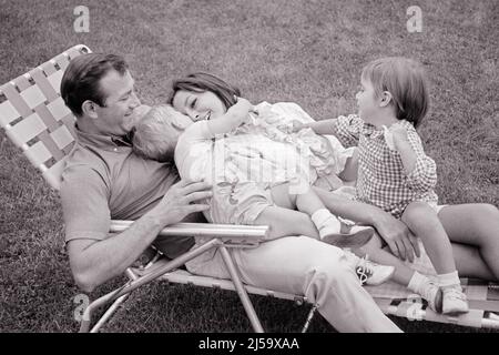 1960S FAMILIE VON 4 LACHEND ALLE AUF DEM GLEICHEN RASENSTUHL IM HINTERHOF LIEGEN ZWEI KINDER KLEINKIND JUNGE UND EIN MÄDCHEN AUF MUTTER UND VATER - J13207 HAR001 HARS MAMA NOSTALGISCHE PAAR 4 VORSTADTMÜTTER ALTE ZEIT ZUKUNFT NOSTALGIE UMARMT ALTE MODE SCHWESTER 1 JUGENDLICH HOF KOMMUNIKATION LACHEN SICHERHEIT JUNGE ERWACHSENE FRIEDEN TEAMWORK UMARMEN STARKE SÖHNE ABSTRAKT ZUFRIEDEN FAMILIEN FREUDE LIFESTYLE FRAUEN VERHEIRATET EHEPARTNER EHEMÄNNER GESUNDHEIT ZU HAUSE LEBEN KOPIEREN RAUM IN VOLLER LÄNGE HALBLANGE UMARMUNG DAMEN TÖCHTER PERSONEN FÜRSORGLICH MÄNNER UMARMEN SCHWESTERN VÄTER B&W PARTNER GLEICHEN GLÜCK WELLNESS KOPF UND SCHULTERN FRÖHLICH Stockfoto