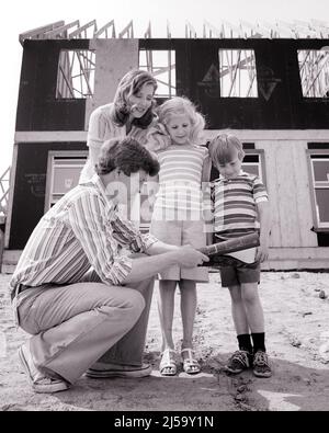 1970S MUTTER VATER UND ZWEI KINDER STEHEN VOR DEM HAUS IM BAU VATER KNIET MIT HAUSENTWÜRFEN - J14171 HAR001 HARS 4 SUBURBANEN MÜTTER ALTE ZEIT NOSTALGIE BRUDER ALTE MODE SCHWESTER JUGENDLICH STIL DESIGN SÖHNE FAMILIEN LIFESTYLE ARCHITEKTUR FRAUEN HÄUSER VERHEIRATET BRÜDER WEBSITE EHEPARTNER EHEMÄNNER HEIM LEBEN KOPIEREN RAUM IN VOLLER LÄNGE HALBLANG DAMEN TÖCHTER PERSONEN WOHN MÄNNER GEBÄUDE GESCHWISTER SCHWESTERN BLUEPRINTS VÄTER B&W PARTNER KNIEND STRUKTUR NEUES HAUS UND VÄTER AUSSEN NIEDRIGEN WINKEL HÄUSER GESCHWISTER WOHNSITZ MID-ADULT MID-ADULT MANN MID-ADULT FRAU MÜTTER FRAUEN Stockfoto