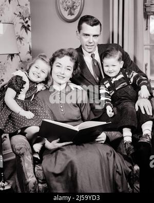 1950S PORTRÄT DER FAMILIE VON VIER LÄCHELNDEN MUTTER HAT BUCH IN IHREM SCHOSS LESUNG FÜR JUNGE MÄDCHEN VATER ALLE OFFEN BLICK IN DIE KAMERA - J2014 HAR001 HARS VIER MAMA KLEIDUNG DRINNEN NOSTALGISCHE PAAR 4 VORSTADT STADT IHRE MÜTTER ALTE ZEIT NOSTALGIE BRUDER ALTE MODE SCHWESTER 1 JUGENDLICHE STIL KOMMUNIKATION STARKE SÖHNE ERFREUT FAMILIEN FREUDE LIFESTYLE ZUFRIEDENHEIT FEIER FRAUEN VERHEIRATET BRÜDER EHEPARTNER EHEMÄNNER HEIM LEBEN KOPIEREN RAUM HALBLANGE DAMEN TÖCHTER PERSONEN FÜRSORGLICH MÄNNER GELASSENHEIT GESCHWISTER SPIRITUALITÄT SCHWESTERN VÄTER B&W PARTNER LAP AUGENKONTAKT GLÜCK WELLNESS KOPF UND SCHULTERN FRÖHLICHE FREIZEIT Stockfoto