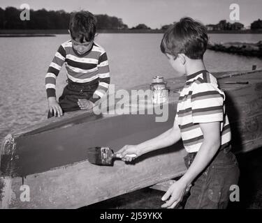 1950S 1960S ZWEI ANONYME JUNGEN BRÜDER IN GESTREIFTEN T-SHIRTS UND JEANS MALEN DEN RUMPF EINES RUDERBOOTES DINGHY AM SEE - J5005 HAR001 HARS VORBEREITUNG FREUNDSCHAFT HALBLANGE INSPIRATION MÄNNER GESCHWISTER VERTRAUEN DENIM FESTSETZUNG B&W ZIELE ERFOLG LAKESIDE ZEIT WEG GLÜCK ABENTEUER CHORE REISE UND KURZURLAUB ERHOLUNG STOLZ EINES DER FERIEN RUDERBOOT GESCHWISTER REPARATUR VERBINDUNG KONZEPTIONELLE T-SHIRTS ANONYME BLAUE JEANS KOOPERATION BEIBOOT RUMPF INFORMELL JUGENDLICHE SEITEN AUFGABE ZWEISAMKEIT TWILL FERIEN SCHWARZ-WEISS BEILÄUFIG KAUKASISCHE ETHNIE HAR001 ALTMODISCH Stockfoto