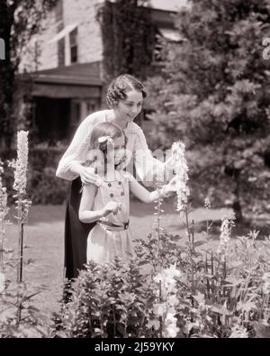 1930S LÄCHELNDE FRAU MUTTER UND TOCHTER IM GARTEN, DIE BLÜTEN AUF DIGITALIS PURPUREA ODER EINER GEWÖHNLICHEN FUCHSHANDSCHUHPFLANZE UNTERSUCHEN - J4735 HAR001 HARS NOSTALGIE ALTE MODE 1 JUGENDLICHER STIL STARK ZUFRIEDEN FAMILIEN FREUDE LIFESTYLE FRAUEN HÄUSER HAUS LEBEN KOPIEREN RAUM HALBLANGE DAMEN TÖCHTER PERSONEN WOHN PFLEGE GEBÄUDE PFLANZEN B & W SOMMER GÄRTNER FRÖHLICH UND GEMEINSAME UNTERSUCHUNG HÄUSER LÄCHELT GÄRTEN FREUDIGE RESIDENZ ODER PERSÖNLICHE ANHAFTUNG ZUNEIGUNG BLÜTEN EMOTION FÜCHSE HANDSCHUH JUGENDLICHE MITTLEREN ERWACHSENEN MITTLEREN ERWACHSENEN FRAU MÜTTER PRE-TEEN PRE-TEEN MÄDCHEN SAISON SCHWARZ UND WEISS KAUKASISCH ETHNISCHE ZUGEHÖRIGKEIT HAR001 Stockfoto