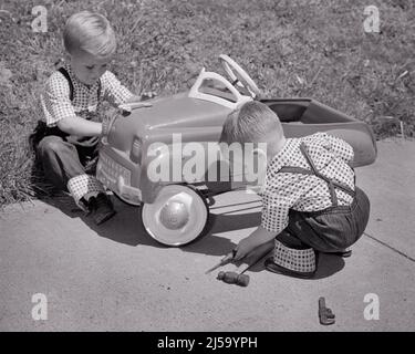 1950S ZWEI JUNGEN ZWILLINGSBRÜDER IN PASSENDEN OUTFITS SPIELEN AUTO MECHANIKER BEFESTIGUNG EINES SPIELZEUGAUTOS - J5404 HAR001 HARS LIFESTYLE BRÜDER HAUS LEBEN KOPIEREN RAUM FREUNDSCHAFT GANZKÖRPERMATCH MÄNNER GESCHWISTER VERTRAUEN FIXIERUNG TRANSPORT S & W ZIELE ENTSPRECHEN GLEICHEN GLÜCK HOCH WINKEL-OUTFITS ERHOLUNG EIN GESCHWISTER REPARATUR PEDLE KONZEPTUELLE STILVOLLE BABY JUNGE LOOK-ALIKE KOOPERATION DUPLICATE WACHSTUM JUGENDLICHE LOOK ALIKE PRÄZISIONSAUFGABE ZWEISAMKEIT SCHWARZ-WEISS KAUKASISCHE ETHNIE KLON HAR001 ALTMODISCH Stockfoto