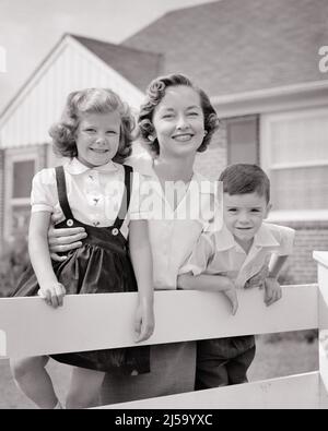 1950S PORTRAIT LÄCHELNDE MUTTER UND ZWEI KINDER JUNGE UND MÄDCHEN, DIE SICH VOR DEM VORSTADTHAUS AUF EINEN WEISSEN ZAUN STÜTZEN BEI DER KAMERA - J6119 HAR001 HARS MÜTTER ALTE ZEIT NOSTALGIE LEHNTE MEDIEN ALTE MODE SCHWESTER 1 JUGENDLICHE SÖHNE ERFREUT FAMILIEN FREUDE ZUFRIEDENHEIT FRAUEN HÄUSER GESUNDHEIT HEIM LEBEN FREUNDSCHAFT HALBWERTIG DAMEN TÖCHTER PERSONEN WOHN AUSSCHNITT MÄNNER GEBÄUDE VERTRAUEN SCHWESTERN B&W AUGE KONTAKT GLÜCK FRÖHLICH UND STOLZ HÄUSER LÄCHELT VERBINDUNG FREUDIGE RESIDENZ KOOPERATION WACHSTUM MITTE ERWACHSENE MÜTTER ZWEISAMKEIT SCHWARZ UND WEISS HAR001 ALT MODISCH Stockfoto