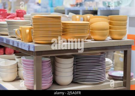 Gerichte werden im Laden verkauft. Reihen von verschiedenen gelben Schüsseln und Tellern für Zuhause auf Regalen in einem Supermarkt. Stockfoto