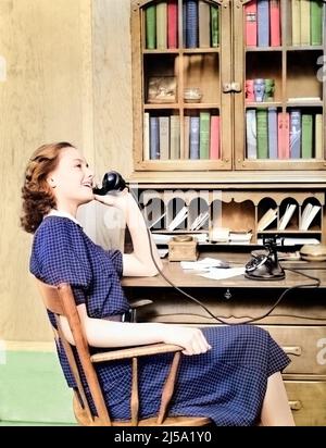 1930S 1940S TEENAGER-MÄDCHEN AM SCHREIBTISCH SITZEN GESPRÄCH AUF ALTEN SCHWARZEN DREHWAHLTELEFON - T5280C HAR001 HARS STILVOLLE BÜCHERREGAL DREH KAUKASISCHEN ETHNIE HAR001 ALTMODISCH Stockfoto