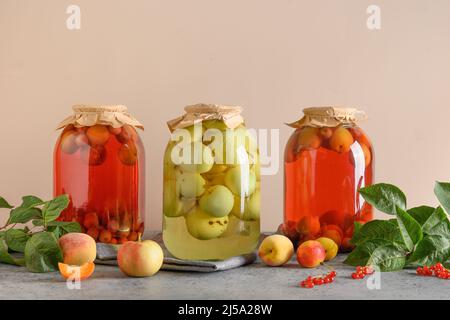 Drei hausgemachte Dosenfrüchte Apfel und Kirsche Kompott in großen Gläsern auf grauen Tisch.Sommer selbst angebaute Ernte und Konserven. Stockfoto