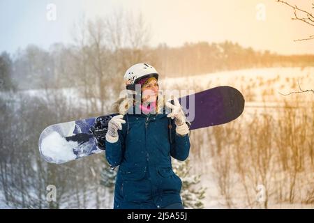 Das Mädchen hält ein Snowboard in den Händen, sie trägt eine Bergjacke und einen Helm Stockfoto