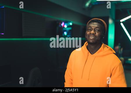 Schöner bärtiger afroamerikanischer Gamer in einem orangen Hoodie nach einem Turnier in einem Internetcafe. Hochwertige Fotos Stockfoto