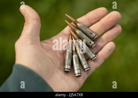 Patronen in der Handfläche. Maschinengewehr Kugeln in der Hand. Schalengehäuse für das Schießen. Einzelheiten zu militärischen Waffen. Aufzählungszeichen von automatisch Stockfoto