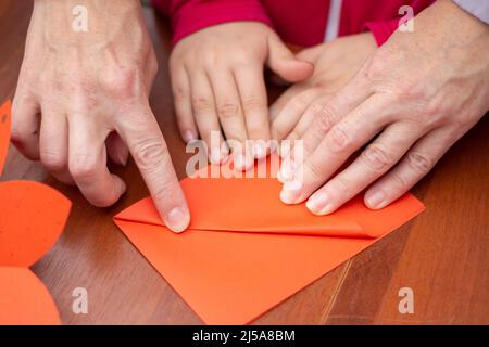 Faltpapier. Unterricht in der Kreativität von Kindern. Kinder und Erwachsene gestalten zusammen einen Umschlag. Co-Creation. Origami-Hintergrund wird ausgeführt. Stockfoto