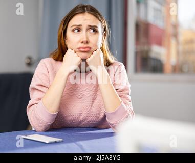 Aufgeregte Frau weinte, während sie am Tisch im Zimmer saß Stockfoto