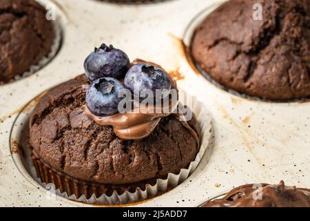 Frisch gebackene Muffins mit Schokoladencreme und Heidelbeeren in einer Keramikpfanne Stockfoto