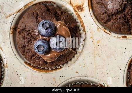Frisch gebackene Muffins mit Schokoladencreme und Heidelbeeren in einer Keramikpfanne von oben Stockfoto