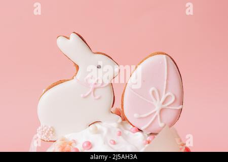Häschen- und Eierkekse auf Kuchen vor rosa Hintergrund Stockfoto