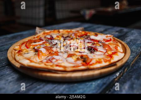 Pizza mit Mais, Fleisch und Tomaten auf einem Hintergrund von Brettern. Stockfoto