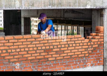 Kemerowo, Russland - 24. juni 2021. Maurer Arbeiter Mauerwerk Ziegel auf Mörtel, Gebäude Trennwand in Gebäude mit Beton Hauptrahmen, selektive FOC Stockfoto