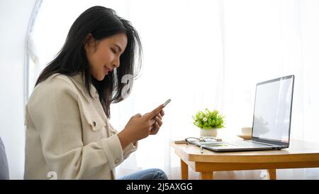 Rückansicht, charmante schöne asiatische tausendjährige Frau sitzt in komfortablen und hellen Café, mit ihrem Smartphone. Stockfoto