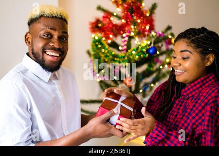 afroamerikanisch glückliches Paar in der Liebe präsentieren eine Geschenkbox im Wohnzimmer Stockfoto