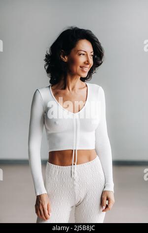 Porträt einer fröhlichen lächelnden Frau in weißer Sportkleidung, hervorgehoben auf einem grauen Hintergrund. Stockfoto