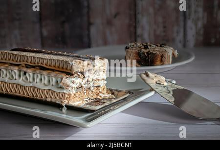 Ein rechteckiger Kaffee-Moka-Eiskuchen auf einem weißen Teller mit einer Scheibe im Hintergrund Stockfoto