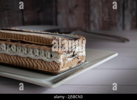 Ein rechteckiger Kaffee-Moka-Eiskuchen auf einem weißen Teller mit einer Vintage-Holzwand im Hintergrund Stockfoto