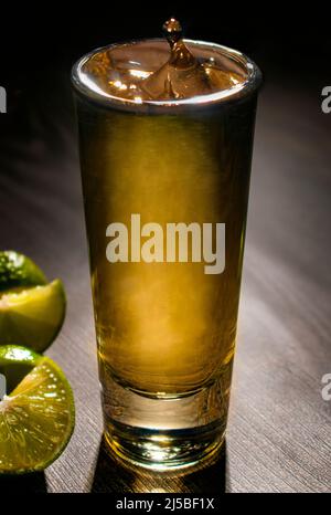 Serviert einen TEQUILA-SCHUSS auf einem Holztisch mit Scheiben grüner Zitrone an der Seite, Makrofotografie Stockfoto