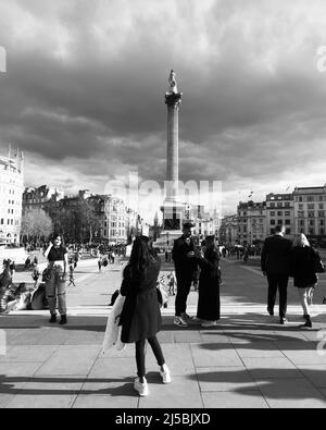 Touristen, die Fotos auf dem Trafalgar Square mit der Nelsons-Säule hinter sich und dem dramatischen Himmel über uns machen. Monochrom. London. Stockfoto