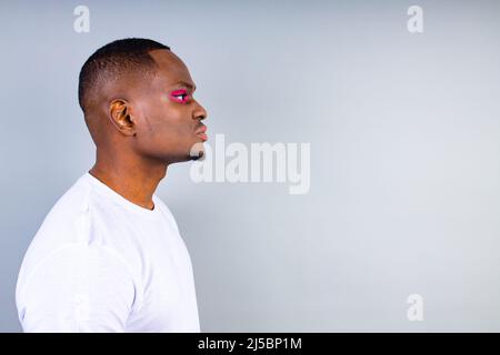 afro-amerikanischer Mann im weißen T-Shirt-Casual-Stil mit rosa Lidschatten und Lippenstift-Crossdressing im Fashion-Show-Studio-Hintergrund Stockfoto